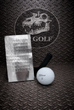 Golf ball and metal card on a textured surface with 'GOLF' branding.