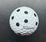 A white golf ball with black dots pattern, featuring the brand 'Titleist' printed on it.