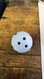 A white golf ball with black trio dot stickers placed on it, resting on a wooden surface.