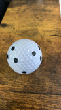 QED trio pattern dots on a white golf ball on a wooden table. 